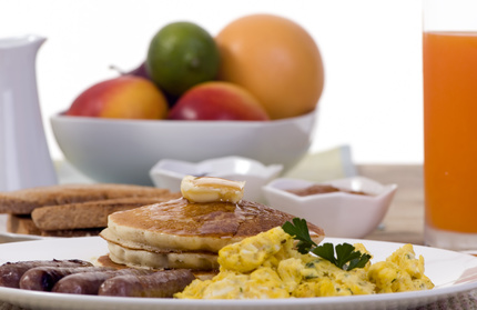 A hearty breakfast plate with pancakes, eggs and sausages.